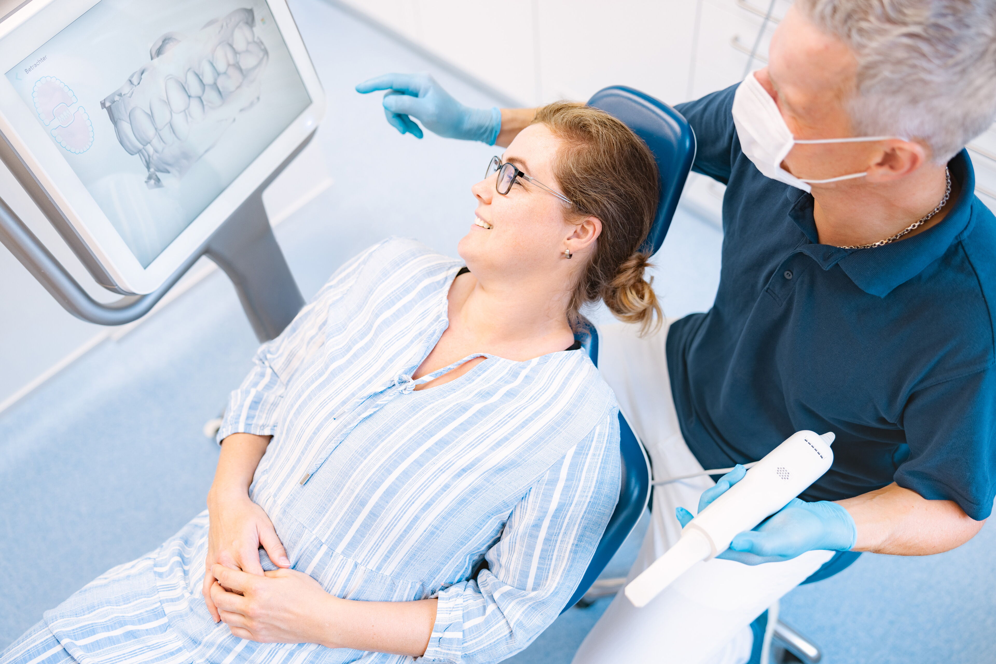 Patientin im Behandlungsstuhl lässt sich das digitale Röntgenbild auf einem Bildschirm in kieferorthopädischen  Praxis erklären.