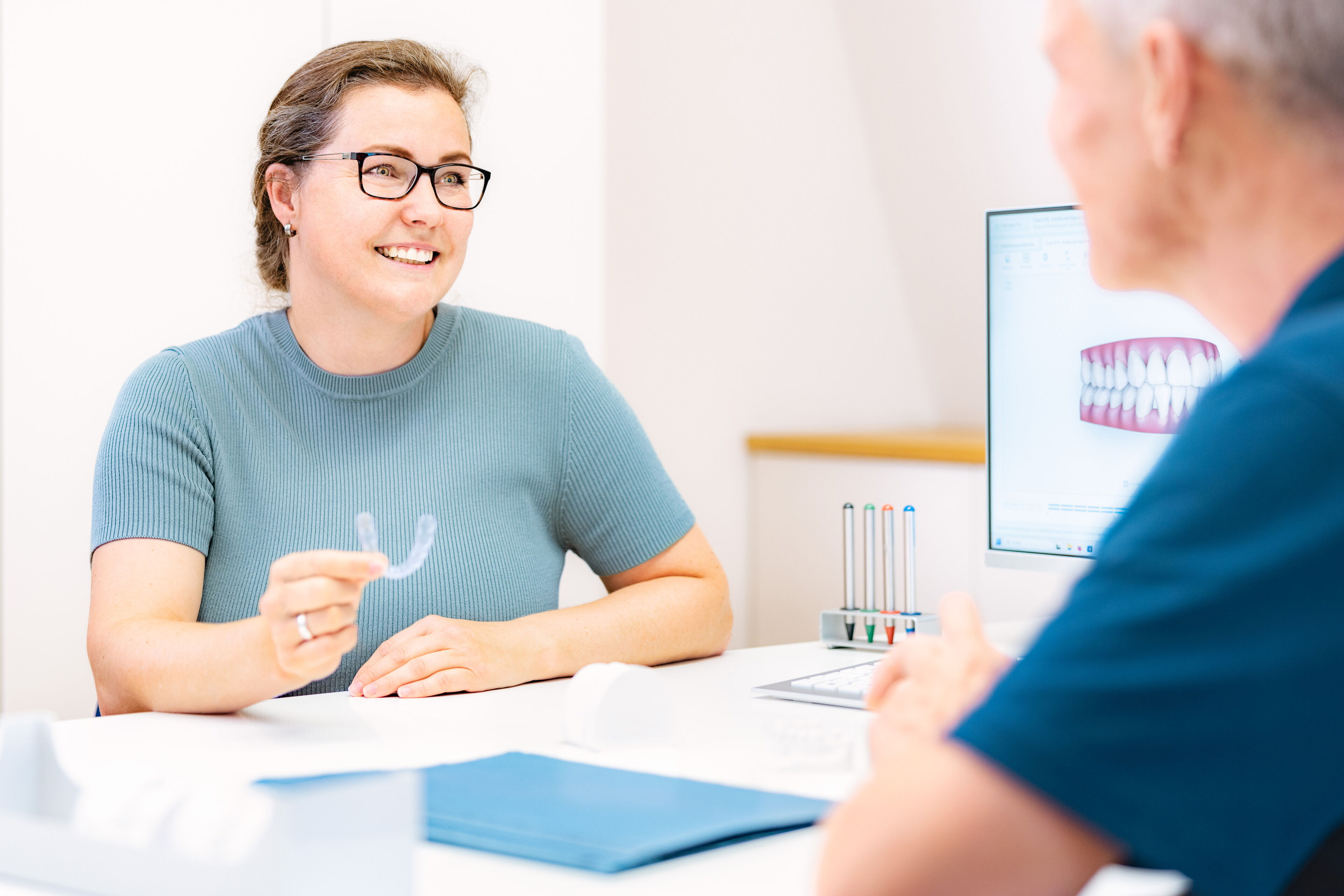 Patientin hält eine transparente Invisalign-Schiene (unsichtbare Zahnspange) während des Beratungsgesprächs in der kieferorthopädischen Praxis Dr. Blümchen in Bielefeld.