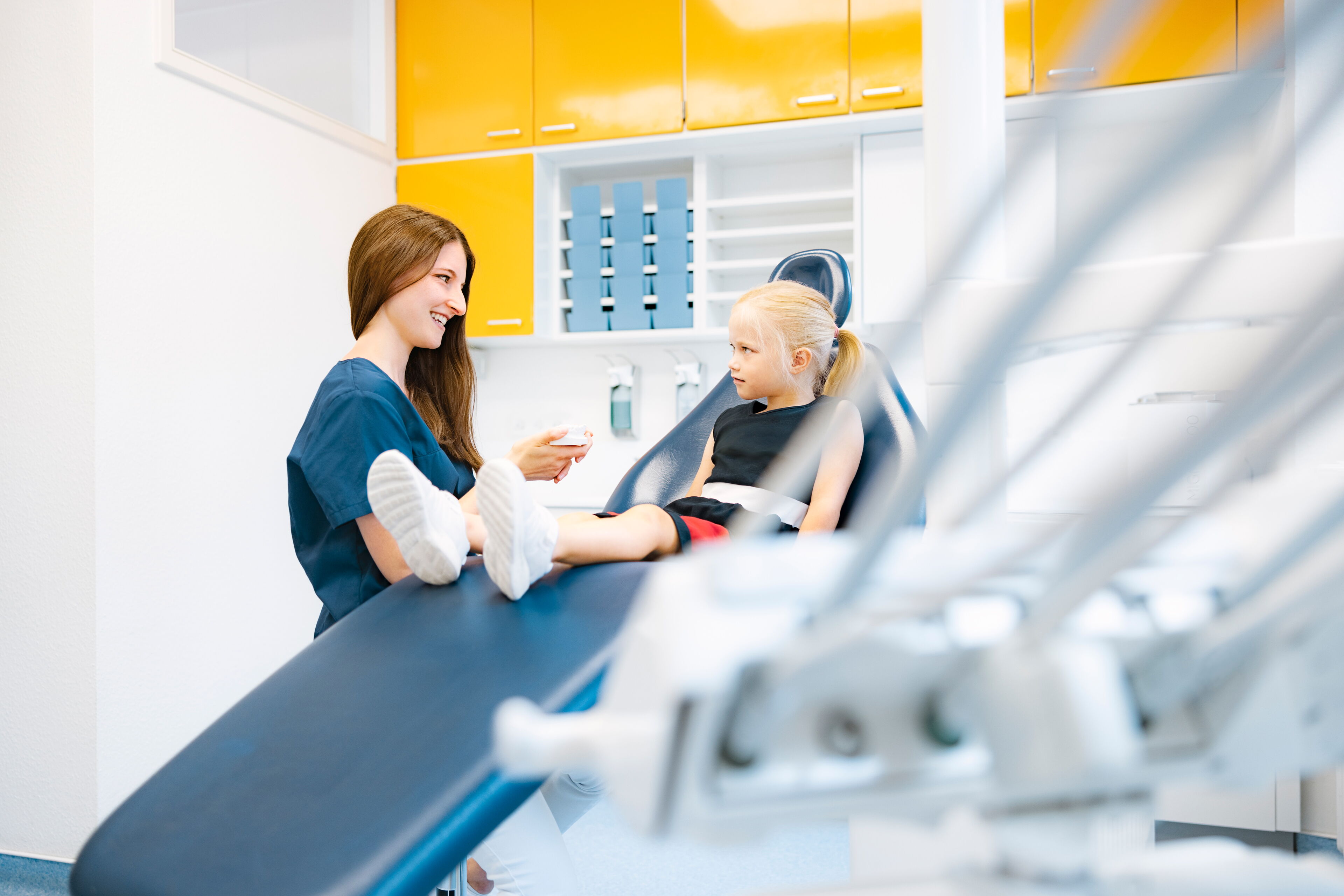 Kleines Mädchen bei der kieferorthopädischen Vorsorgeuntersuchung, begleitet von einer freundlichen Zahnmedizinischen Fachangestellten