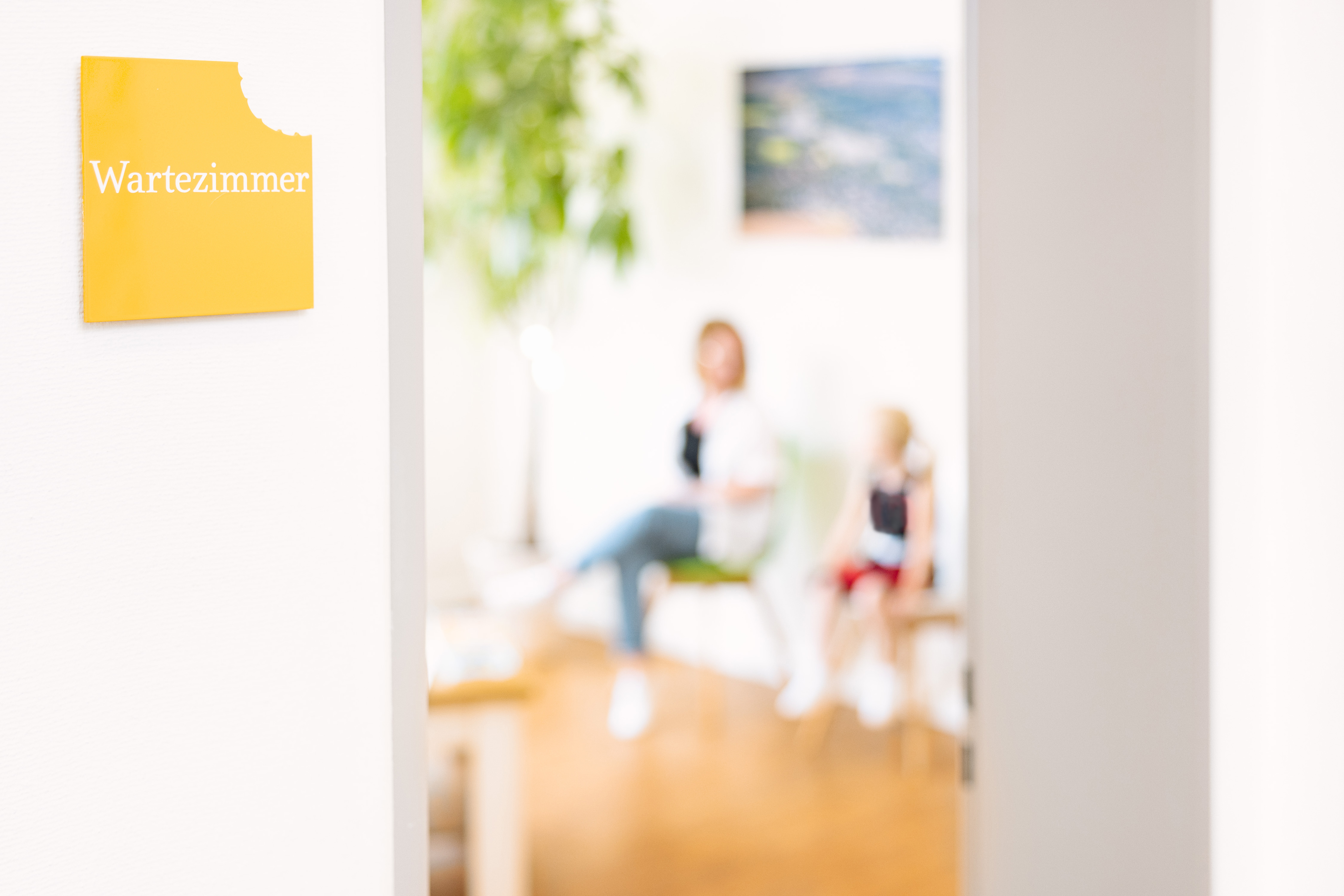 Blick ins Wartezimmer der kieferorthopädischen Praxis Dr. Blümchen in Bielefeld mit Hinweisschild an der Tür und wartenden Patientinnen.